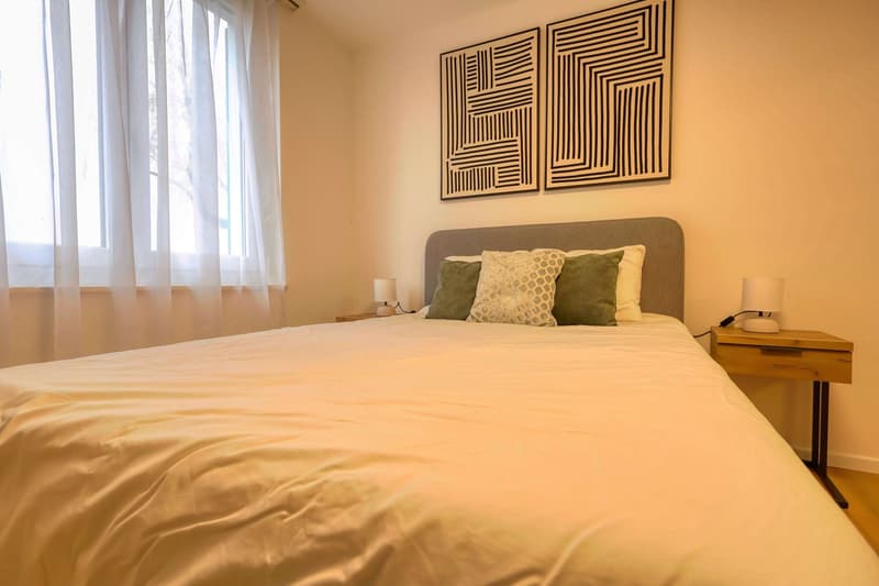 A bedroom with a bed, nightstands, lamps, and a window with curtains.