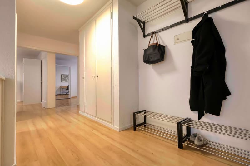 Empty room with wooden floor, white walls, closet, coat rack, and shoes on a shoe rack.