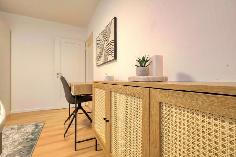 wooden floor, white walls, wooden desk, black chair, wooden cabinet, potted plant, framed picture