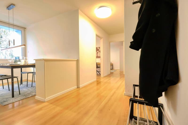 Dining area with table, chairs, and a window. A coat hanging on the wall. A hallway leading to other rooms.