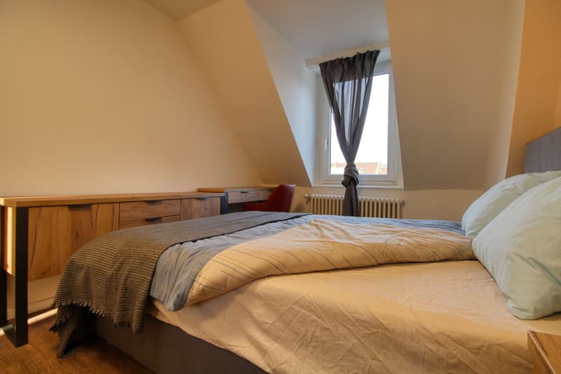 bedroom with bed, wooden cabinet, desk, chair, window, radiator, pillows, blanket