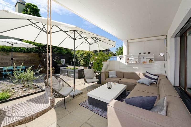 outdoor seating area with sofa, coffee table, and umbrellas, patio, swing, garden with plants, clear view of sky