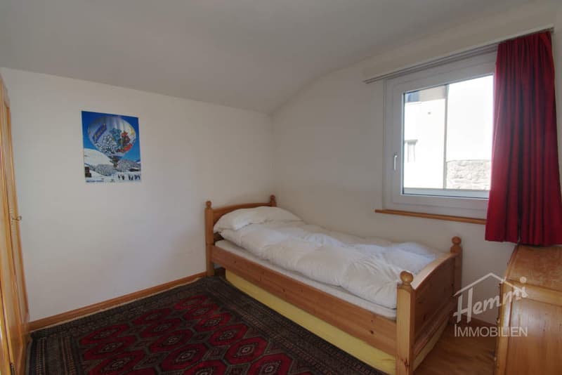 small bedroom with a single bed, rug, window with red curtains, picture on the wall