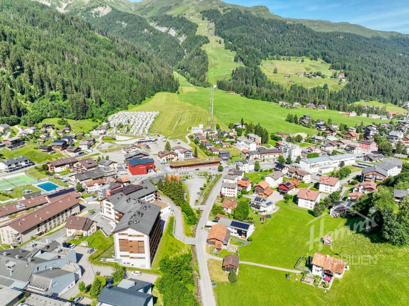 Mountain village with many buildings, green fields, trees, and a tennis court