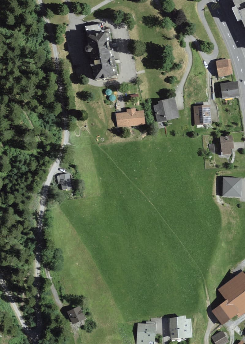 Aerial view of a rural area with several houses, a large green field, and a road.