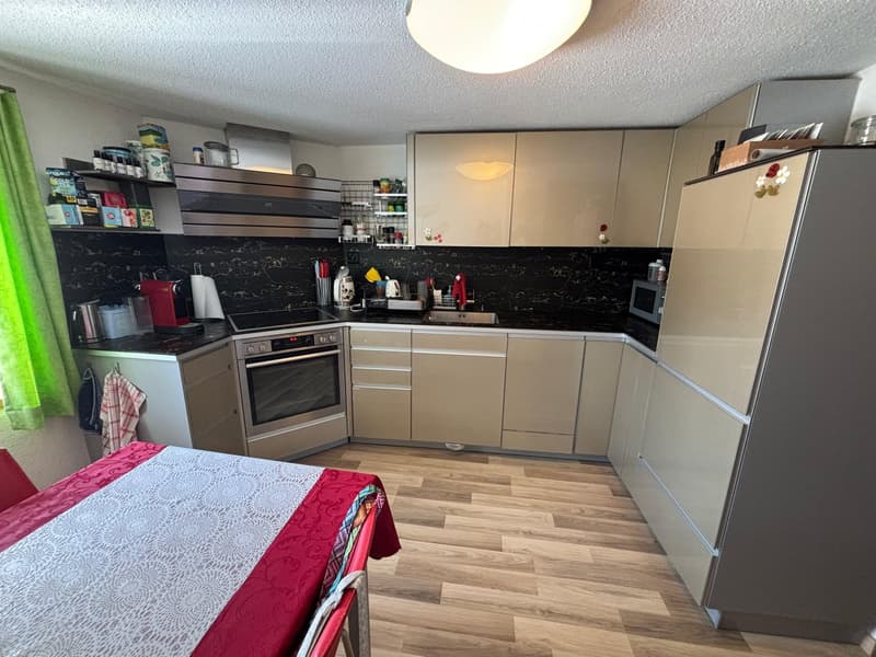 White cabinets, wooden floor, stainless steel appliances, refrigerator, dining table with a cover, open kitchen to the living room