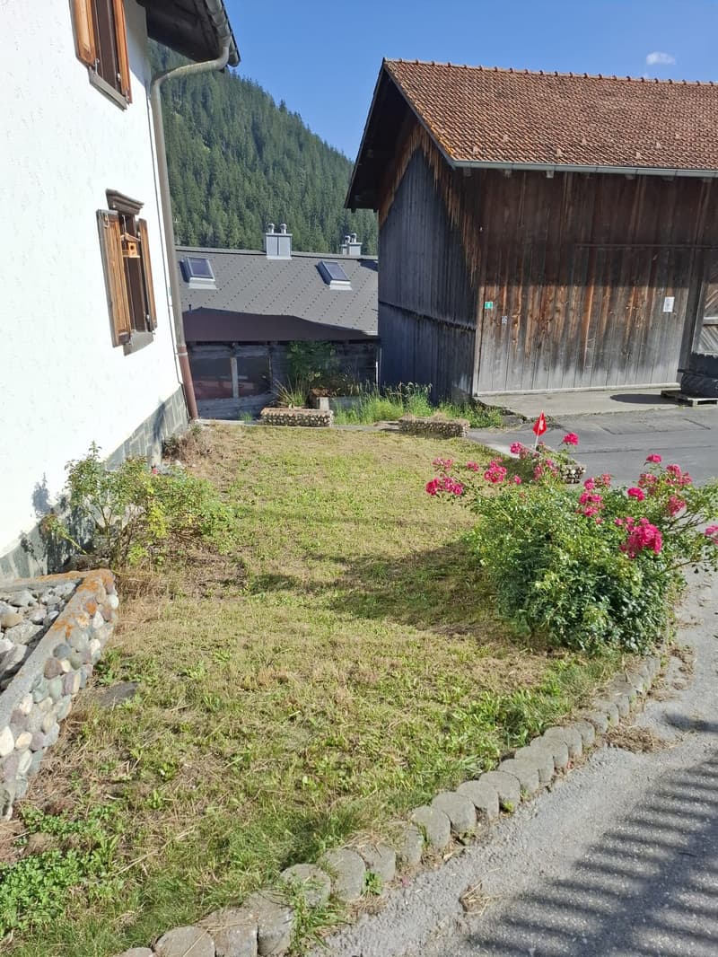 a sloped roof, large window, white wall, wooden barn, mountain view, grass, pink flowers, cobblestone sidewalk