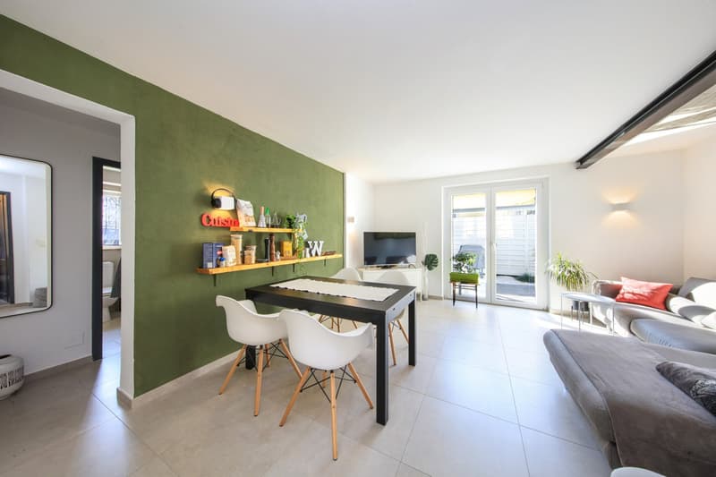 Open-concept living room with green accent wall, dining table, white chairs, TV, and sliding glass door leading to a balcony or terrace