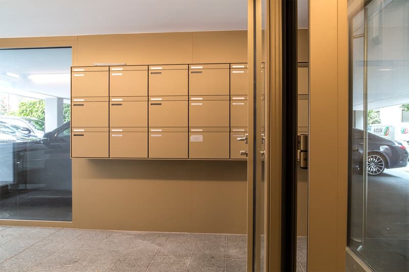 A corridor with beige walls, a glass door, and lockers. A reflection of a car is seen in the glass door.
