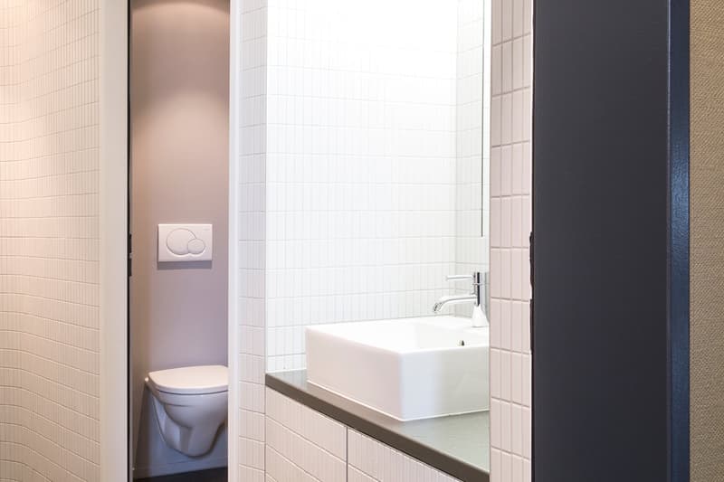 Compact bathroom with white tiles, white countertop, silver faucet, white sink, toilet.