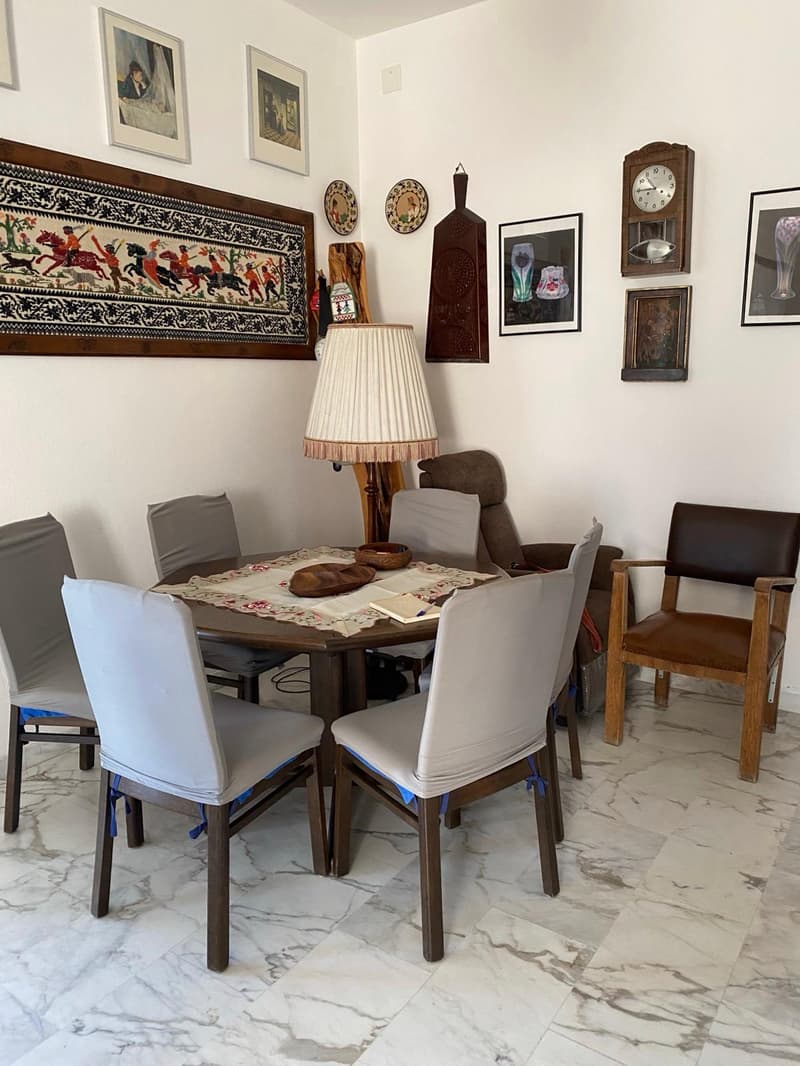 Dining table with chairs, framed artwork on the walls, a floor lamp, and a grandfather clock. The room has a cozy, eclectic decor with a mix of traditional and modern elements.