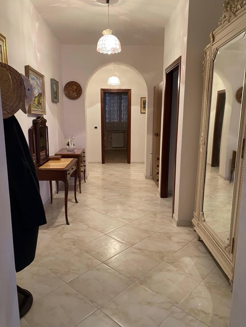 Spacious hallway with marble tile flooring, arched doorways, decorative wall art, and a fireplace visible in the background.