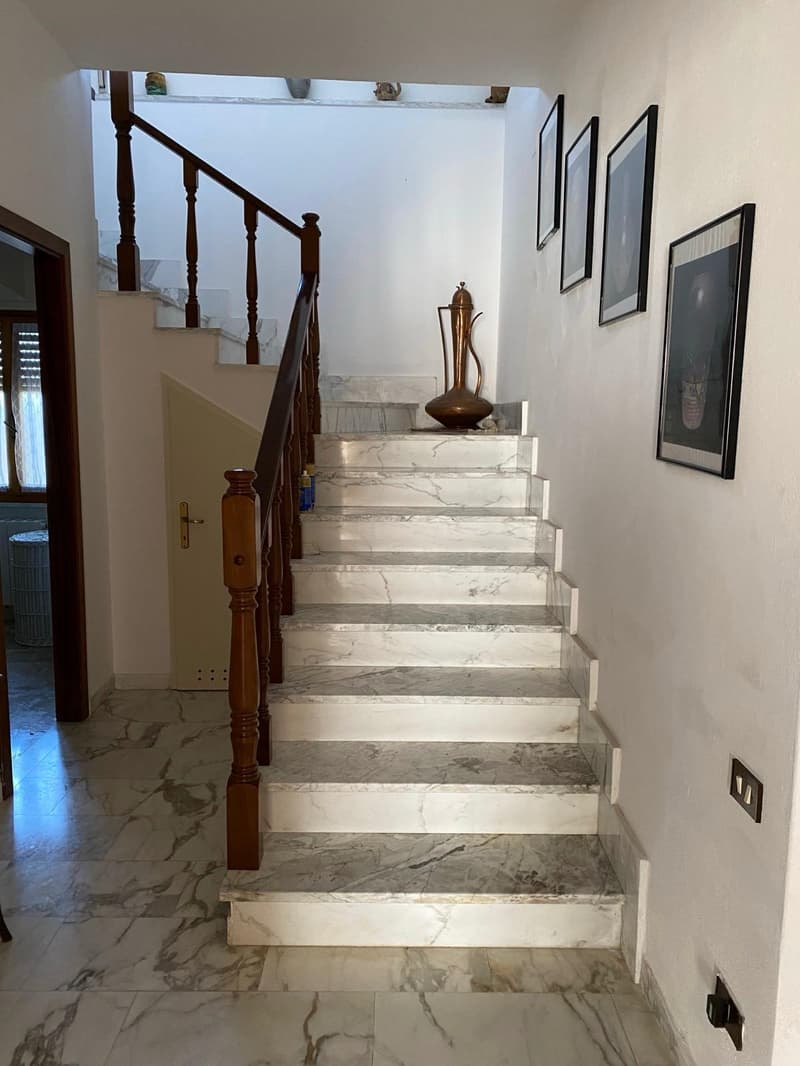 Marble staircase with wooden railings, decorative vase on a shelf, framed artwork on the walls