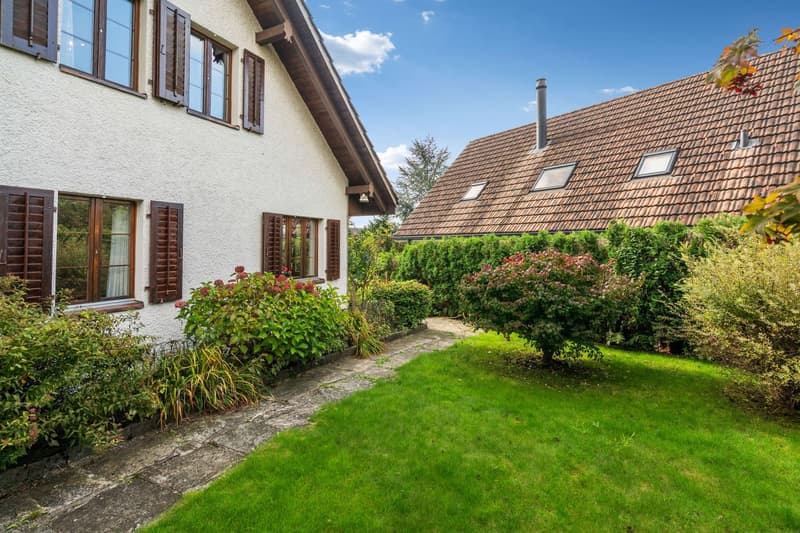 Two houses with a grassy front yard, brick roof, chimney, plants, shrubs, and hedges.