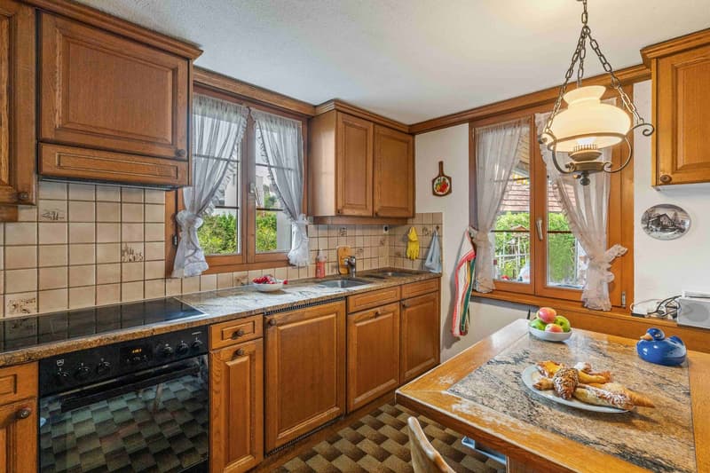 Kitchen with wooden cabinets, granite countertops, gas stove, sink, and chandelier.