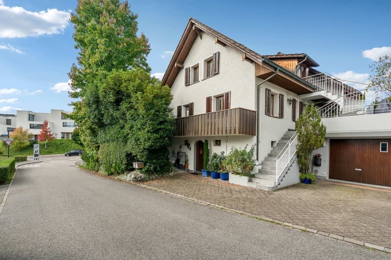 3-story house, white walls, brown roof, balcony, garage, garden, shrubs, trees