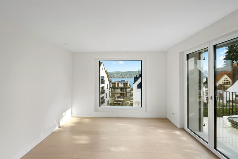 Empty room with wooden floor, large glass windows, balcony, view of the city and lake