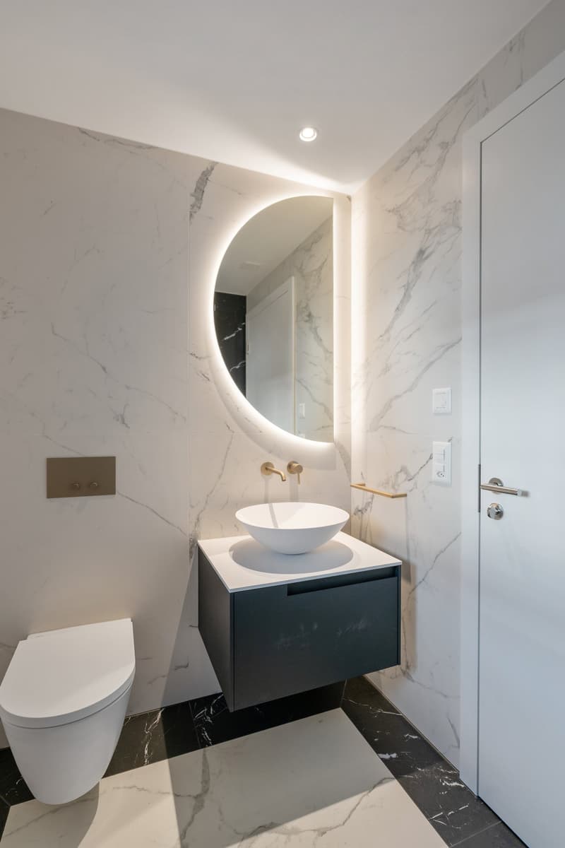 modern bathroom with white marble walls, black marble floor, white sink, round mirror, white toilet