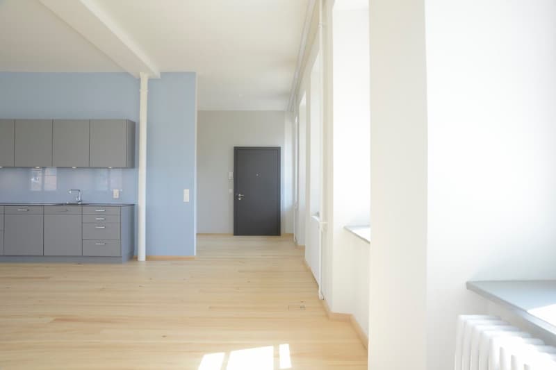 Empty room with wooden floor, blue wall, gray cabinets, white walls, door, radiator, and a sink with faucet.