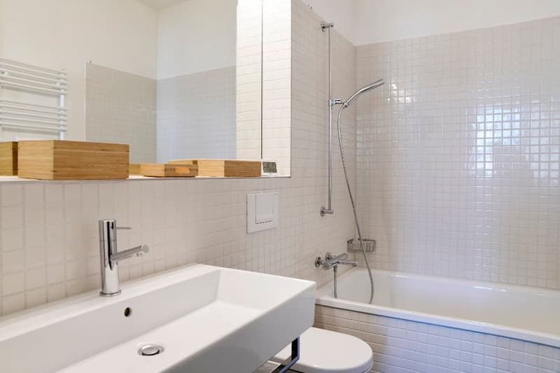 modern bathroom with white tiles, bathtub, toilet, sink, mirror, wooden shelves, towel rack