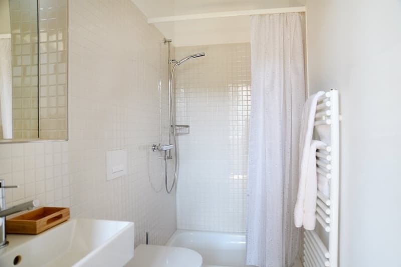 white tiles, white shower curtain, white sink, white toilet, white towel rack
