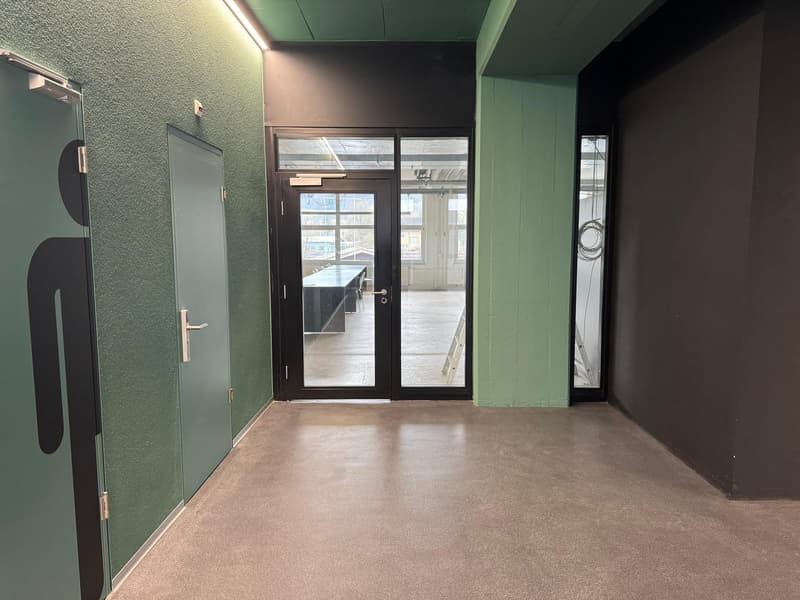 The image shows an interior office space with green walls, a black door with a glass panel, and a concrete floor. The space appears to be a commercial or industrial setting, potentially used as an office or workspace.