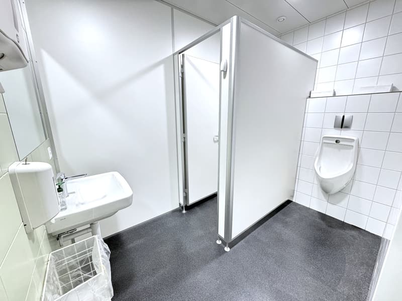 A bathroom featuring white tiles, a sink, a mirror, two stalls, and a urinal.