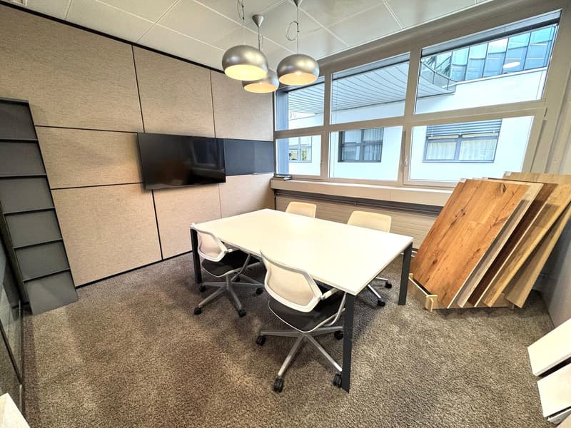 white table, office chairs, hanging lamps, carpeted floor, flat screen tv on wall, large windows
