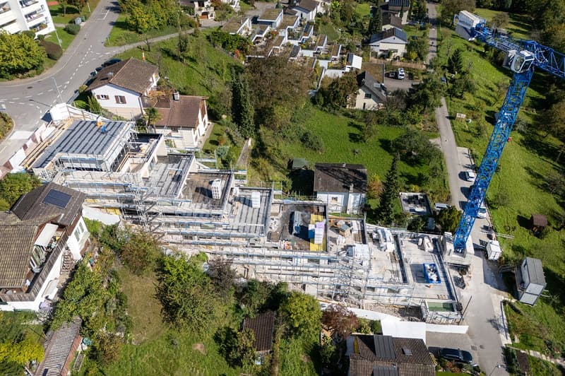 Under construction 3 stories house with brown roof, solar panels, surrounded by houses, small garden, road, parking area, crane