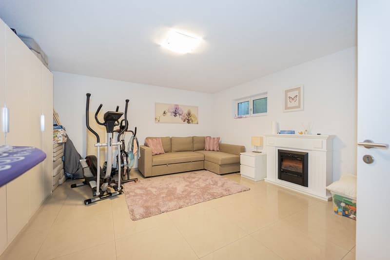 Modern living room with beige floor, white walls, beige couch, beige carpet, exercise machines, window, fireplace