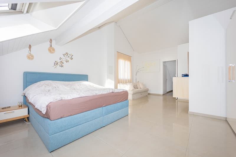 white tiled floor, a blue headboard, large bed, white nightstand, couch with pillows, decorative lights, white walls, arched ceiling