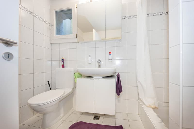 modern bathroom with white tiles, toilet, sink with cabinet, shower curtain