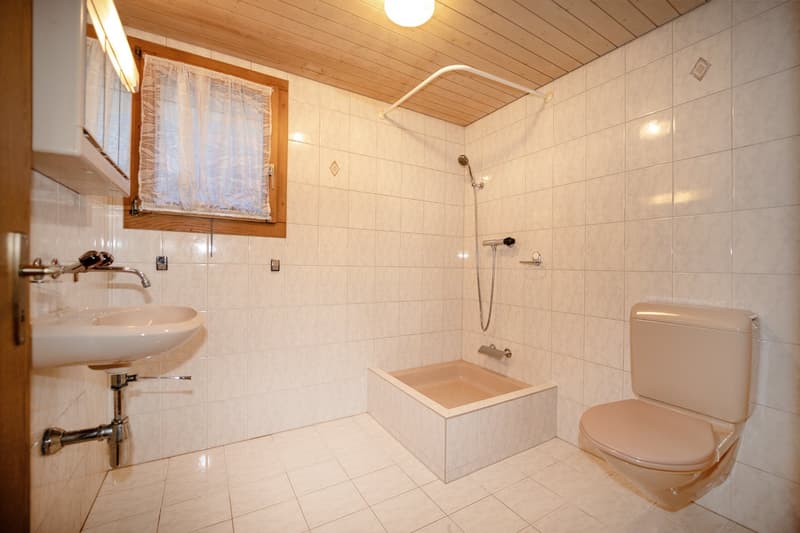 Bathroom with toilet, sink, bathtub, window, wooden ceiling, white tiles