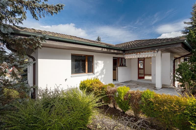 Detached house with tiled roof, white walls, wooden window frames, two windows, front porch with canopy, and a garden with various plants.