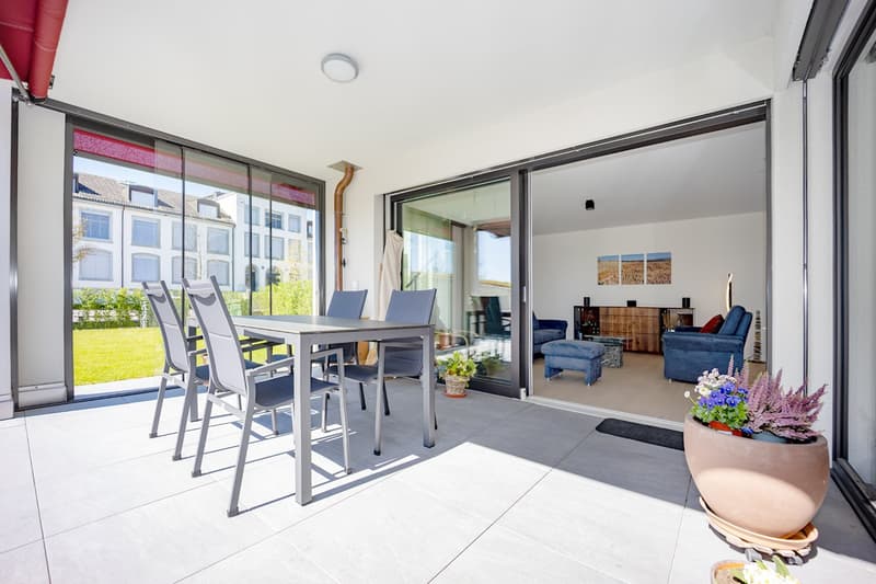 modern patio with table and chairs, sliding glass doors, potted plants, view of a grassy area and a building