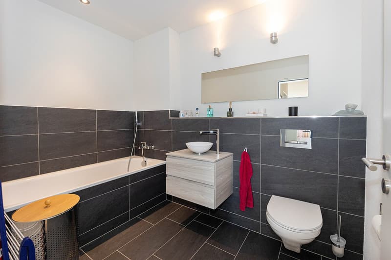 Bathroom with bathtub, sink, toilet, mirror, towel rack, and tiled walls and floor.