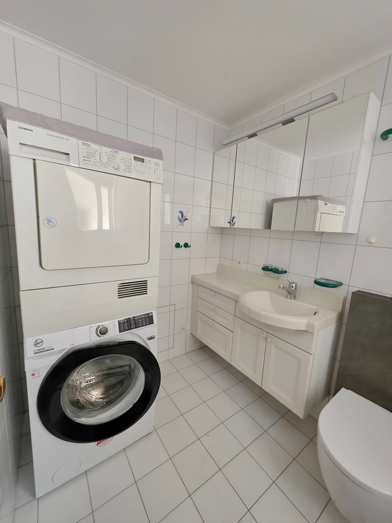 white tiled floor, white cabinets, sink, toilet, washing machine, dryer, mirror