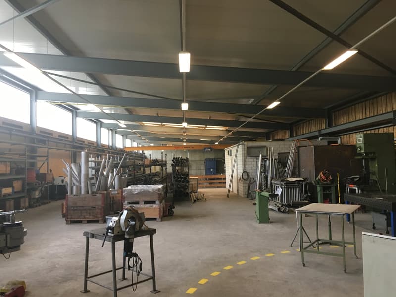 spacious workshop with multiple storage racks, shelves, workbenches, various machinery and equipment, high ceiling with industrial lighting, yellow markings on the floor