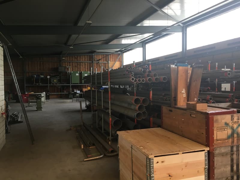 large warehouse with many racks, metal pipes, boxes, ladder, wooden storage boxes