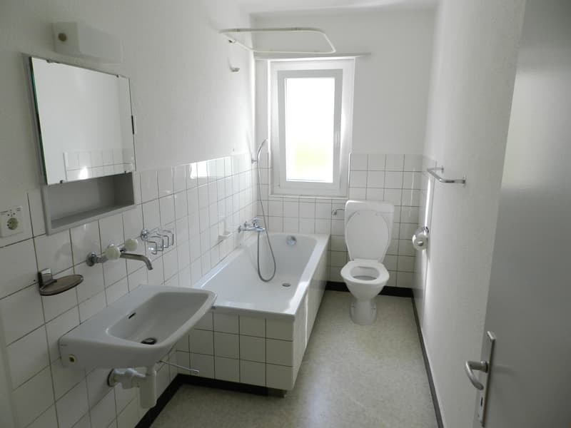 white walls and tiled floor, bathtub with shower, sink, mirror, toilet, and power outlet