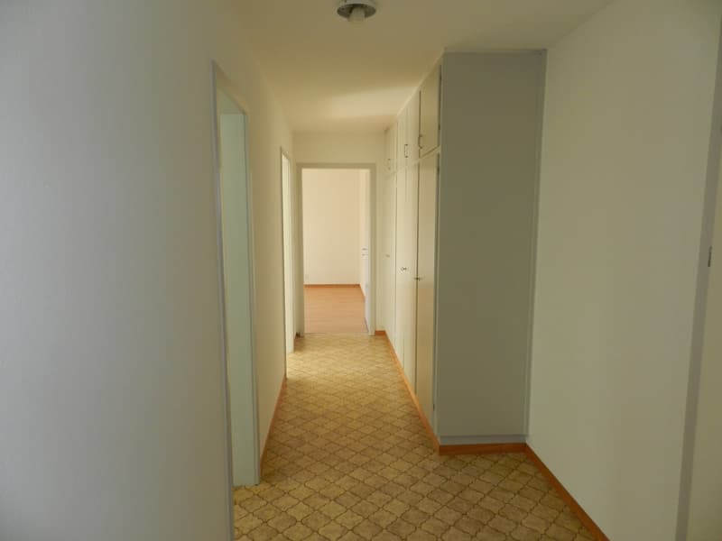 Empty hallway, white walls, tiled floor, closed doors, wooden floor visible