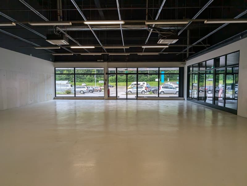 Empty room, concrete floor, large windows, parking area visible through windows