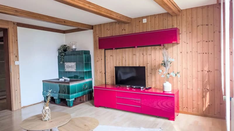 Spacious living room with wooden walls and beams, a large pink TV stand, a green tiled fireplace, and a wooden coffee table.