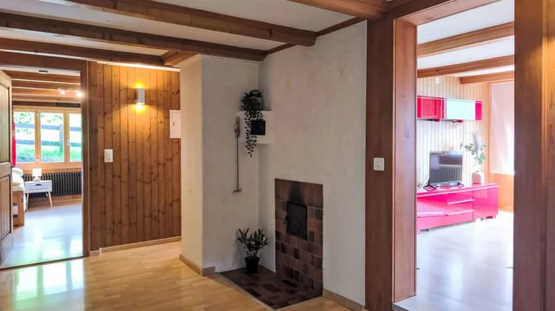 Spacious living room with wooden beams on the ceiling, wood paneled walls, a fireplace, and a pink entertainment unit in the adjacent room