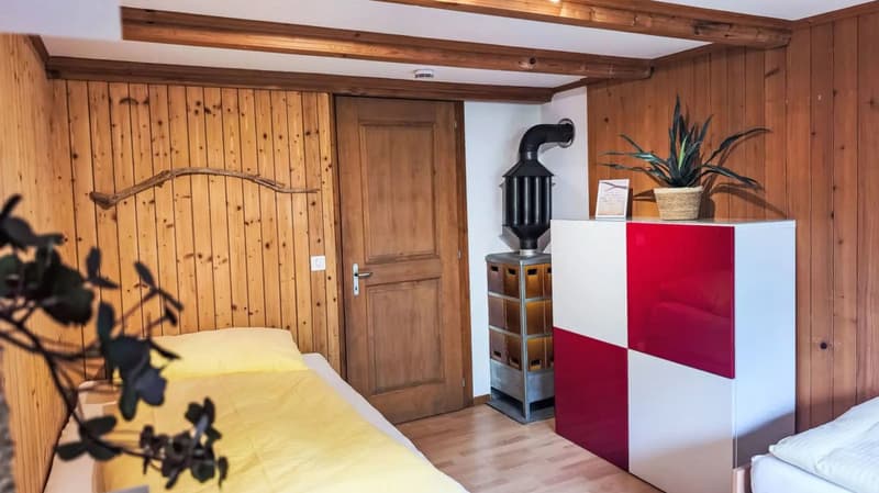 Cozy bedroom with wooden paneled walls, a wooden arched headboard, a red and white cabinet, a potted plant, and a fireplace with a black lantern on top.