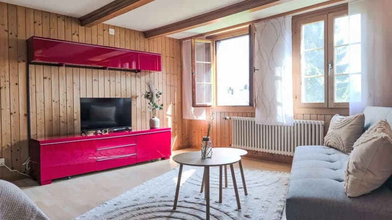 Cozy living room with wooden walls and ceiling, large windows, red TV stand, sofa, coffee table, and decorative elements