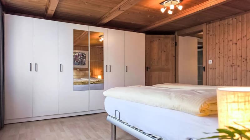 Spacious bedroom with wooden ceiling and walls, large built-in wardrobe, bed, and fireplace