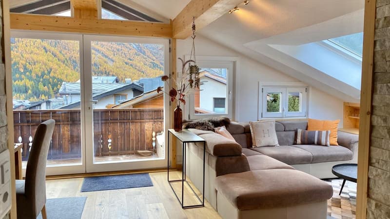 a room with wooden floor, a couch, a coffee table, a chair, a glass door and a wooden balcony