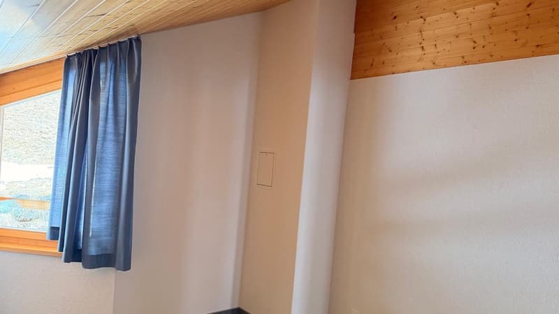 white walls, wooden ceiling, window with blue curtain, power outlet