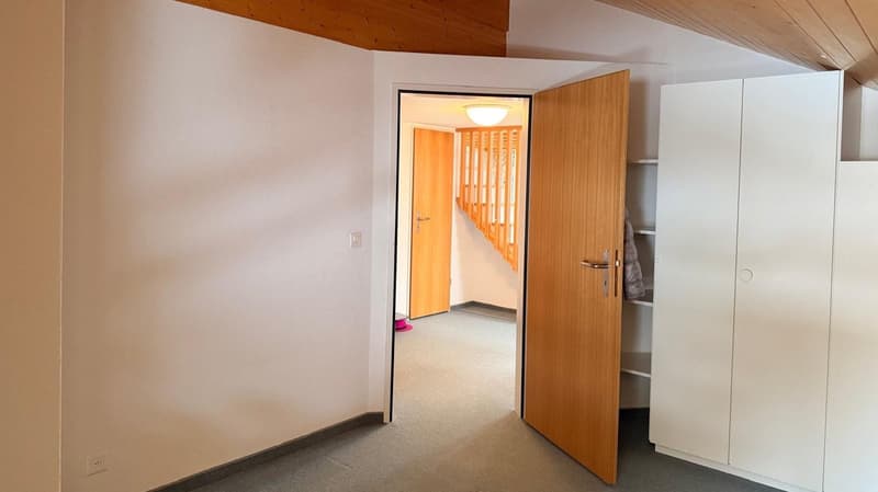 Empty room with wooden door, white walls, wooden ceiling, carpeted floor, closet, and a door leading to a staircase.